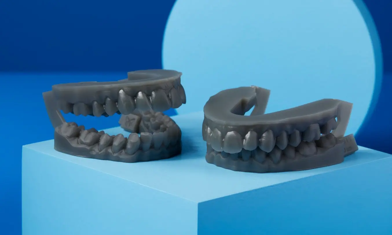 Two 3D-printed grey orthodontic models on a blue background
