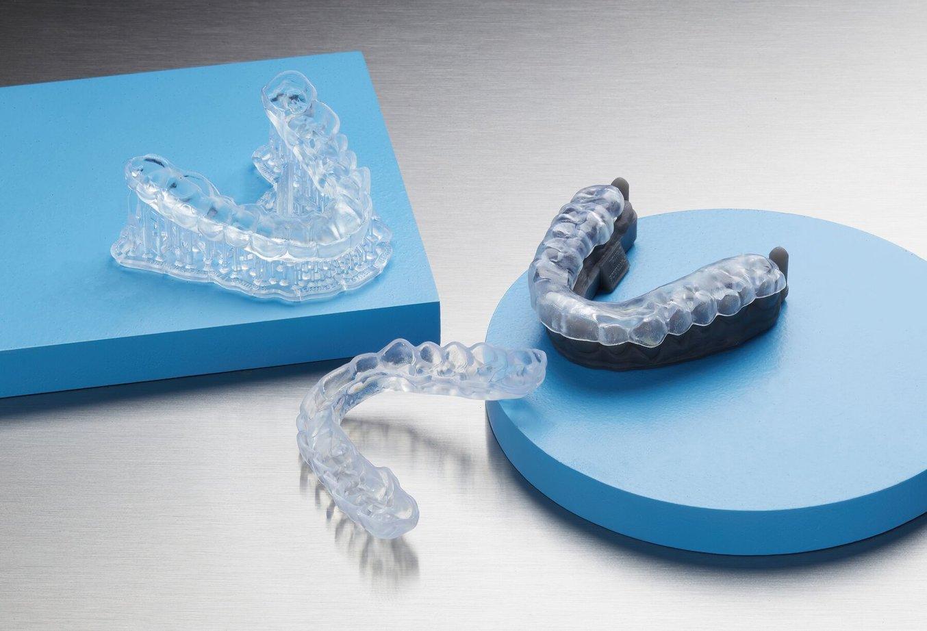 Three clear occlusal splints. One on a model and one still with 3D printed supports attached.