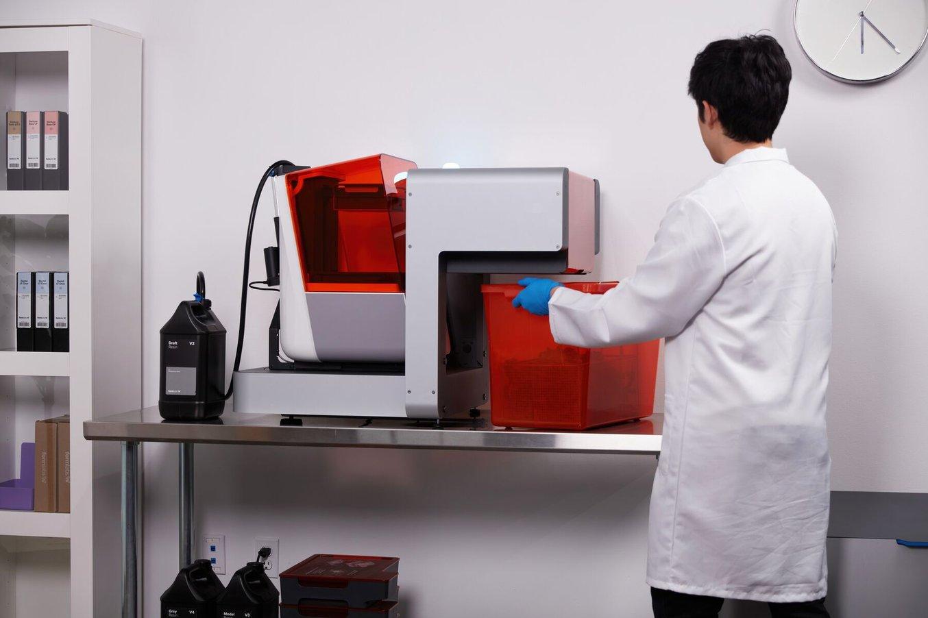 Person in a lab coat removing 3D prints from a Form Auto
