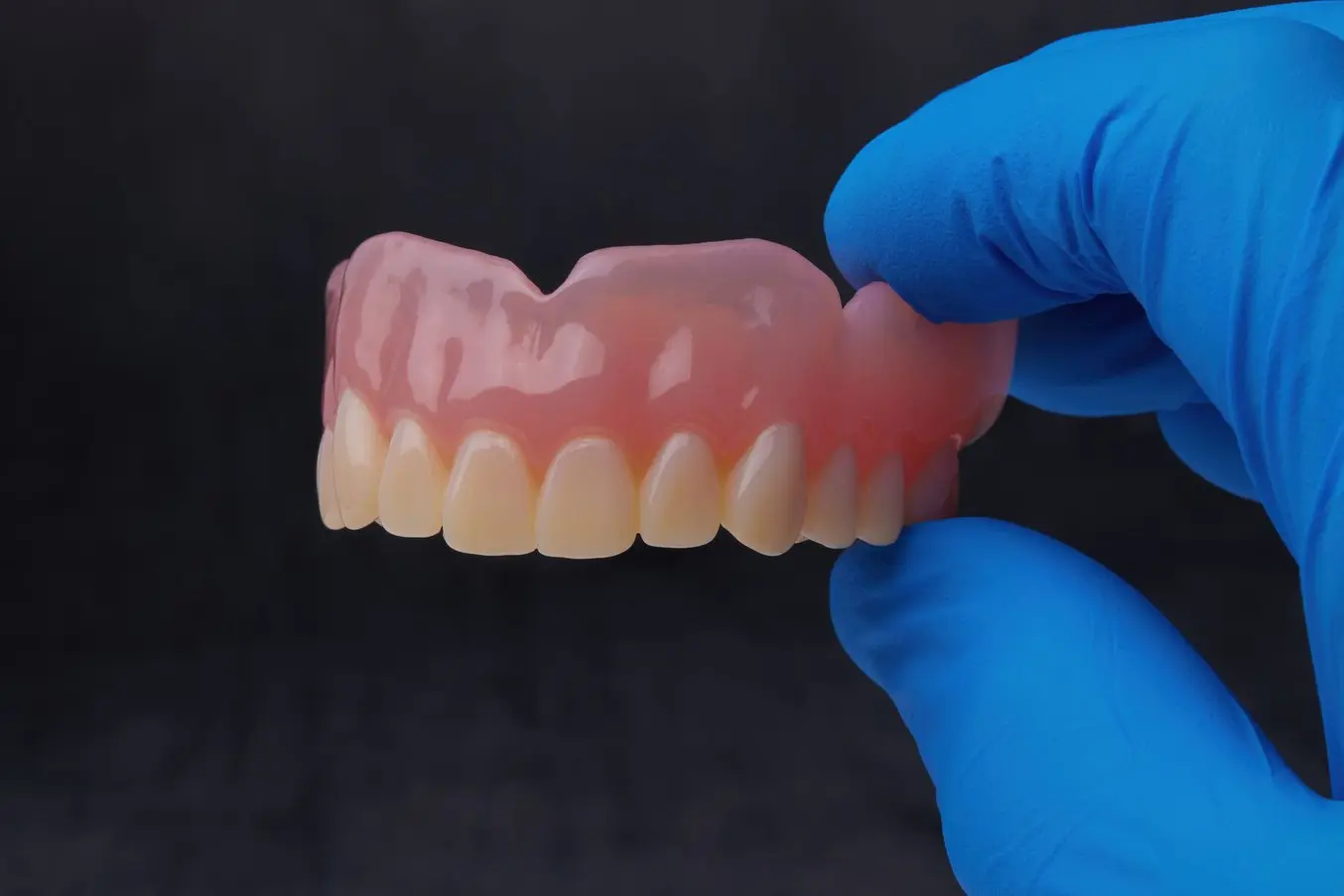 Blue gloved fingers holding a 3D printed denture.