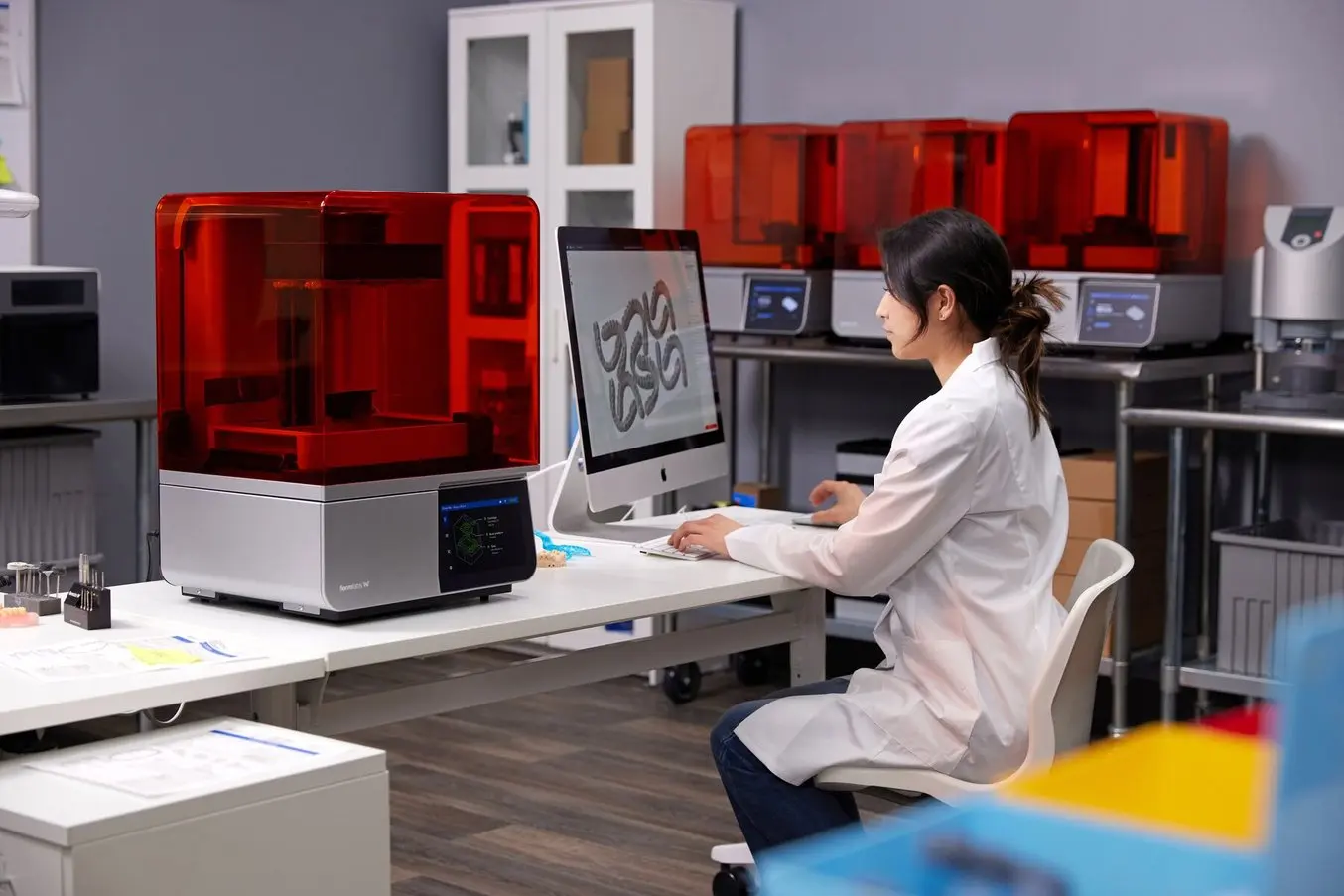 Dental technician works on a computer next to a Form 4B 3D printer