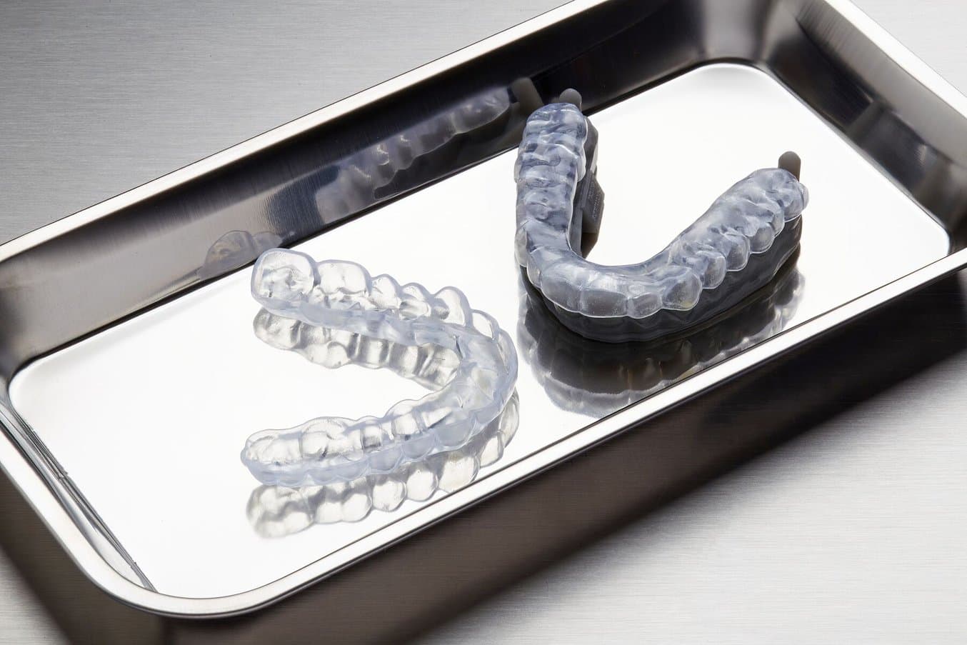 Two clear occlusal splints on metal tray. One is on a model.