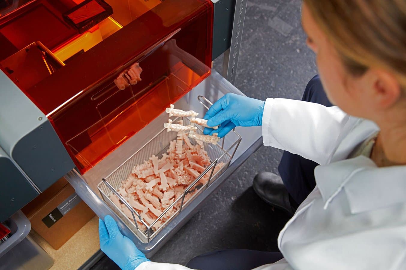 Gloved worker holding 3D printed models in the bin of a Form Auto