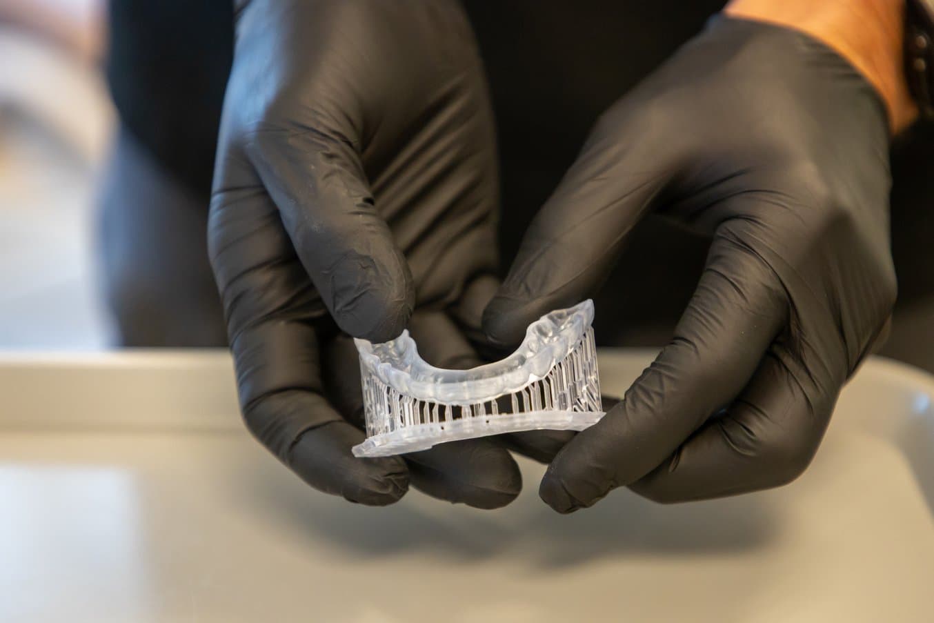 Gloved hands holding a 3D printed occlusal splint on supports