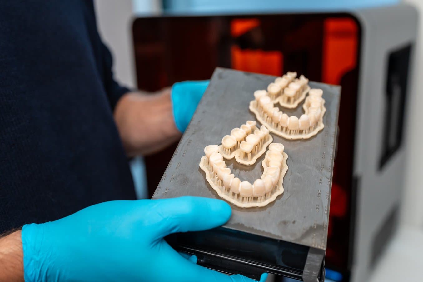 Des restaurations imprimées en 3D sur une plateforme de fabrication soutenues par des mains gantées.