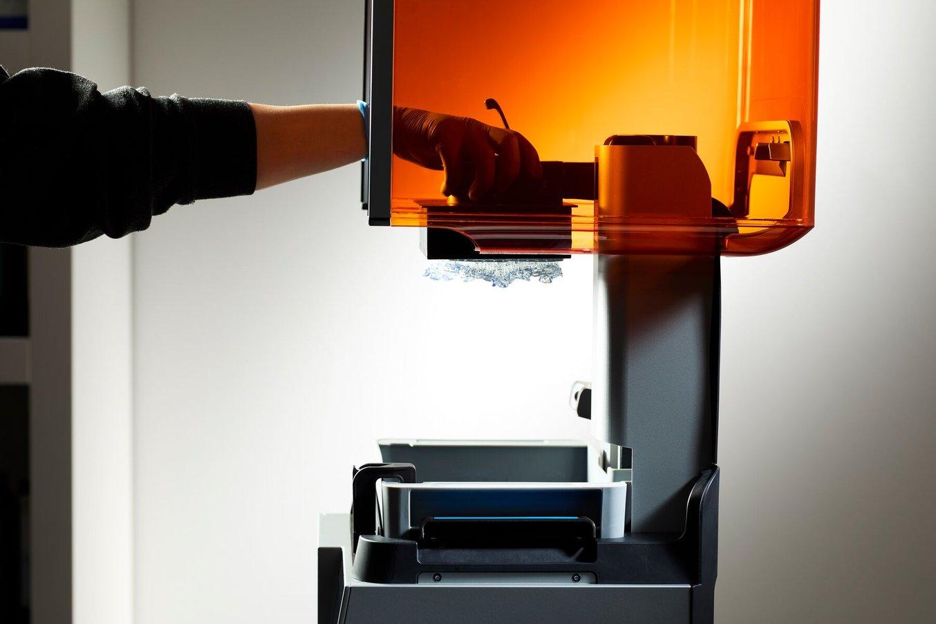 Person reaching inside an open Form 4B printer removing a build platform with prints on it.